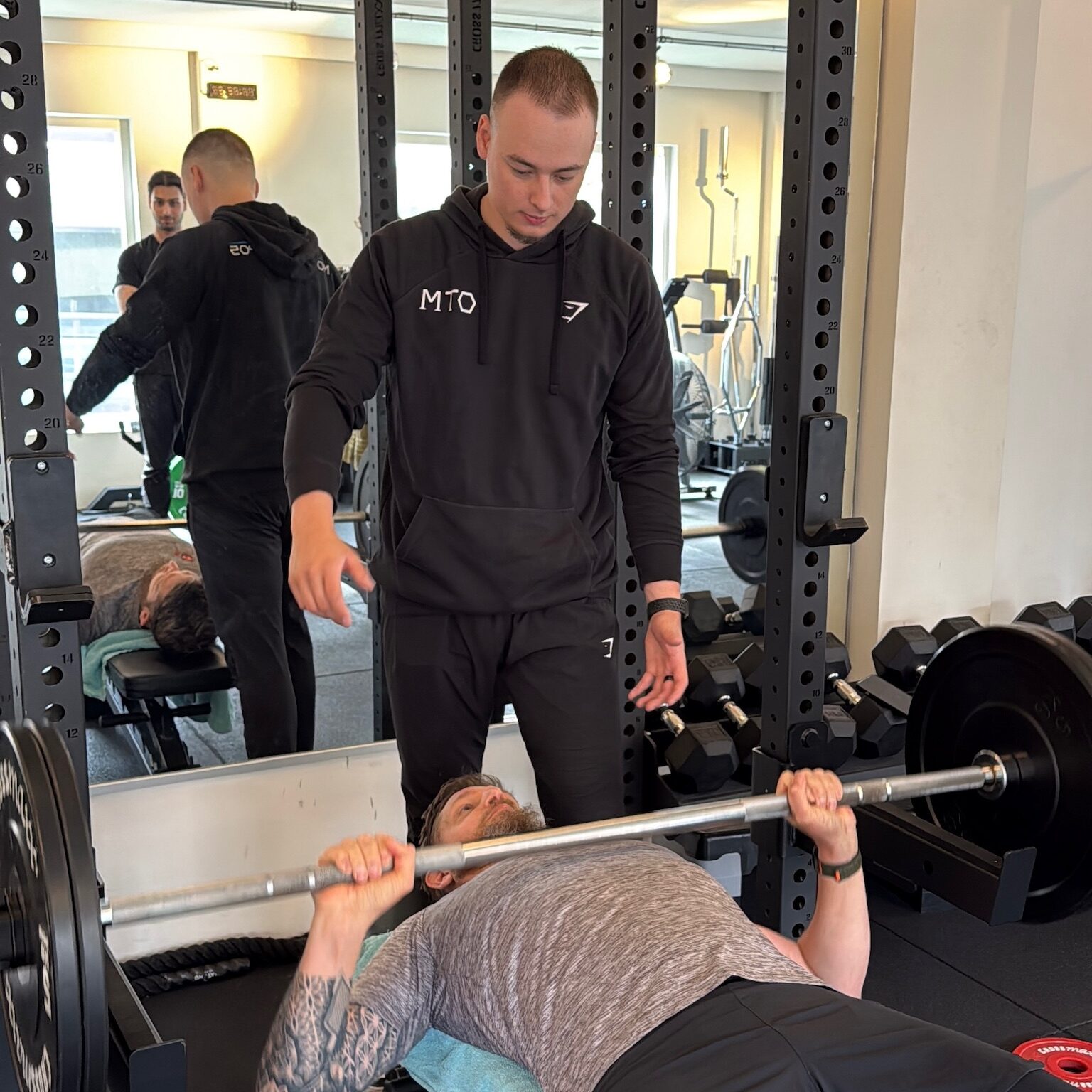 Sporter die met een trainer aan het bankdrukken is.